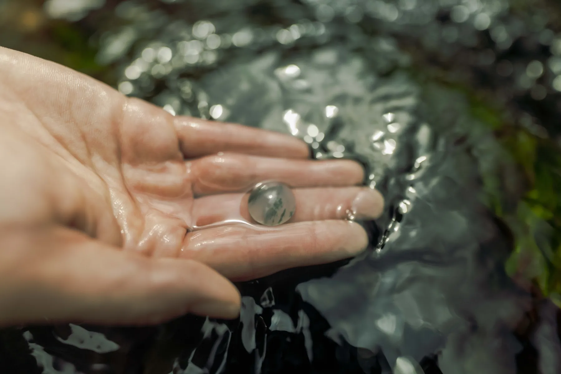 A small jade stone held in an open hand in the river